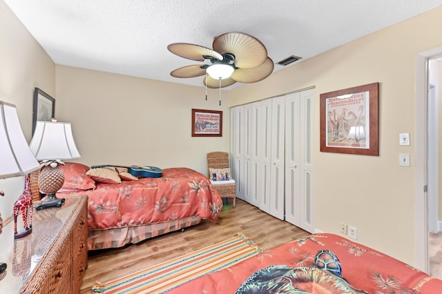 bedroom with a ceiling fan, visible vents, light wood-style floors, a closet, and a textured ceiling