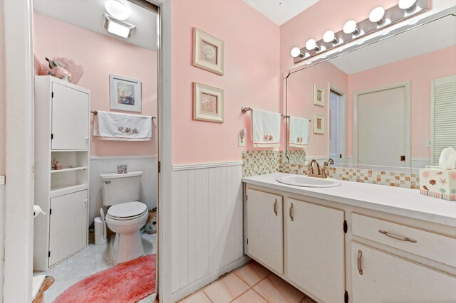 bathroom with tile patterned flooring, toilet, vanity, and wainscoting