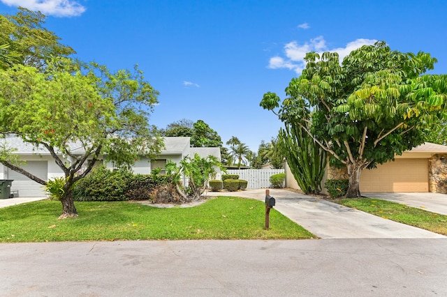 view of front of house with concrete driveway, fence, a garage, and a front lawn