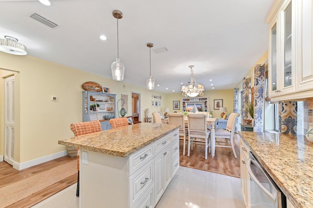 kitchen with visible vents, a kitchen island, light stone countertops, dishwasher, and hanging light fixtures