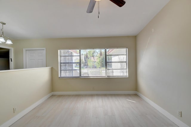 spare room with light wood-style flooring, baseboards, and ceiling fan with notable chandelier