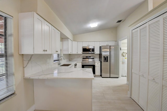 kitchen featuring visible vents, appliances with stainless steel finishes, light stone counters, vaulted ceiling, and a sink