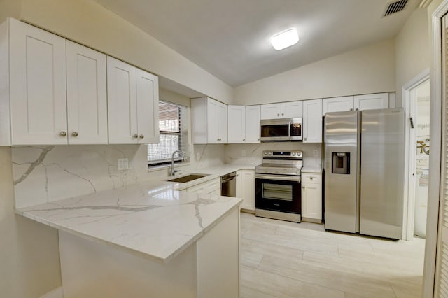 kitchen with a peninsula, a sink, visible vents, vaulted ceiling, and appliances with stainless steel finishes