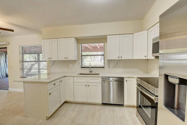 kitchen featuring white cabinets, a peninsula, a sink, stainless steel appliances, and backsplash