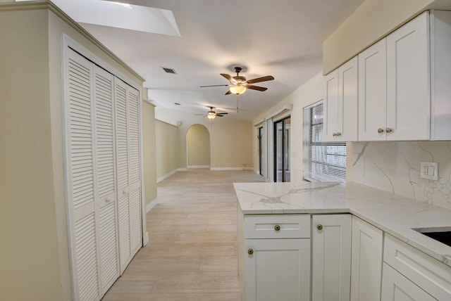 kitchen with arched walkways, backsplash, white cabinetry, light stone countertops, and a peninsula