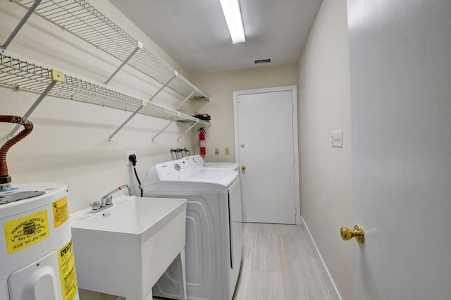 washroom with laundry area, baseboards, washing machine and clothes dryer, water heater, and a sink