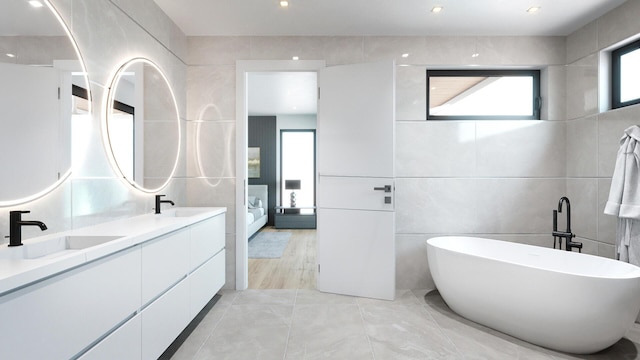 full bath with double vanity, a soaking tub, tile walls, and a sink