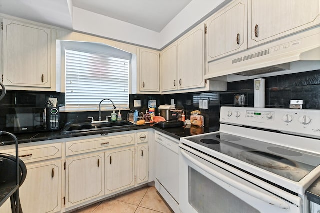 kitchen featuring white appliances, a sink, under cabinet range hood, dark countertops, and backsplash