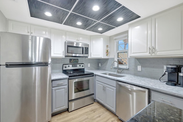 kitchen with a sink, white cabinetry, light wood-style floors, appliances with stainless steel finishes, and light stone countertops