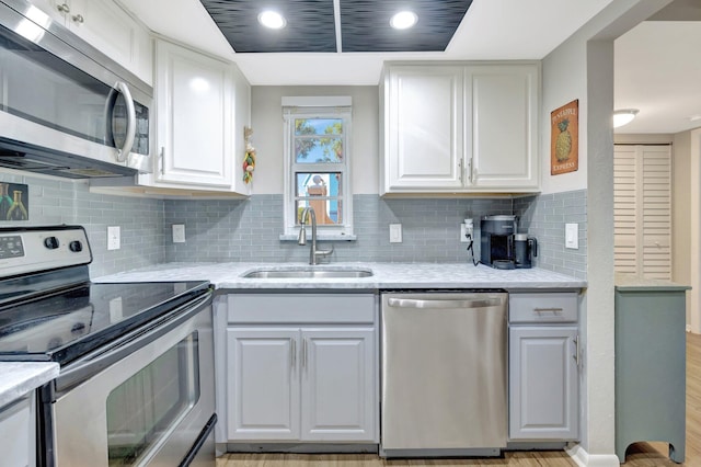 kitchen with light stone countertops, a sink, decorative backsplash, white cabinets, and appliances with stainless steel finishes