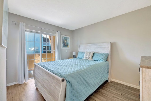 bedroom with access to outside, wood finished floors, and baseboards