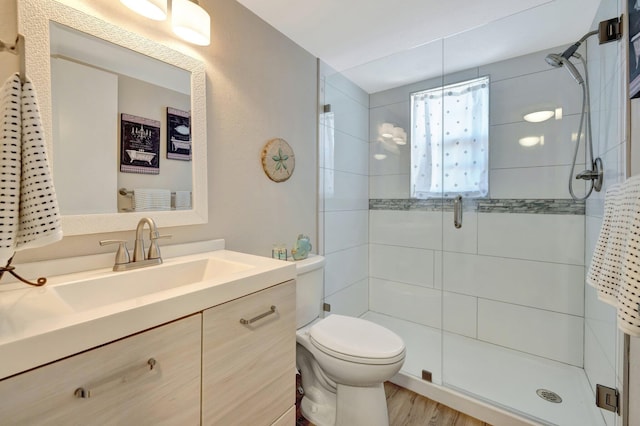 bathroom featuring vanity, toilet, wood finished floors, and a shower stall