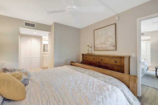 bedroom featuring a ceiling fan, wood finished floors, visible vents, and connected bathroom