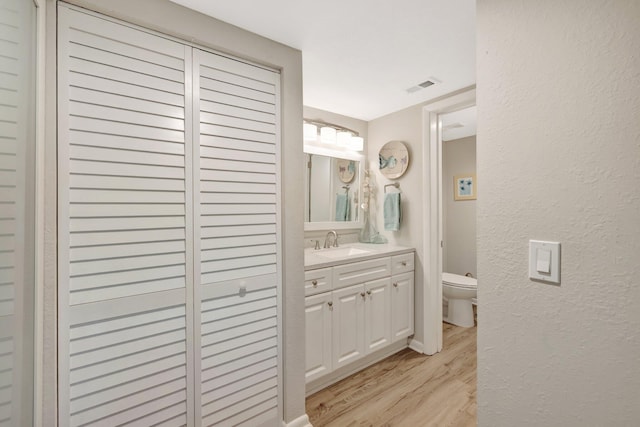 bathroom with toilet, vanity, a textured wall, and wood finished floors