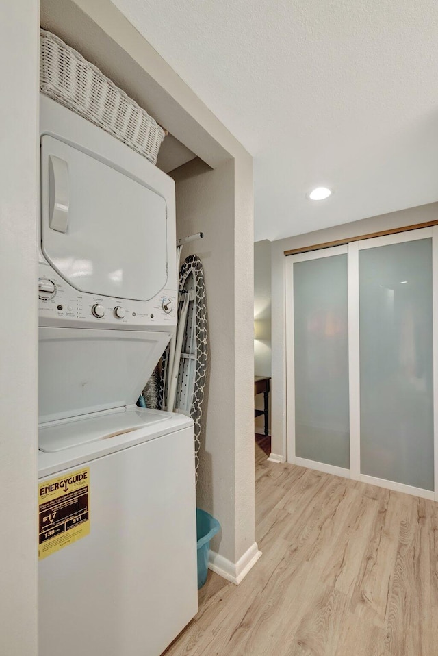 laundry room with a textured ceiling, wood finished floors, stacked washer / drying machine, baseboards, and laundry area