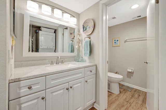 bathroom featuring vanity, wood finished floors, visible vents, stacked washer / drying machine, and toilet