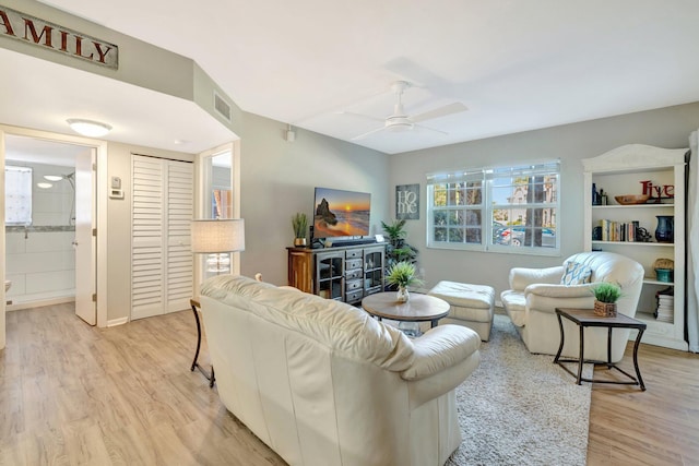 living room featuring light wood-type flooring, visible vents, and ceiling fan