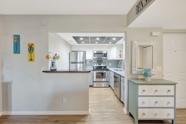 kitchen featuring tasteful backsplash, light wood-type flooring, appliances with stainless steel finishes, white cabinetry, and a sink