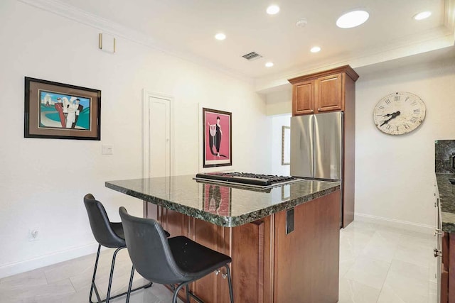 kitchen featuring a center island, dark stone countertops, freestanding refrigerator, brown cabinetry, and gas cooktop