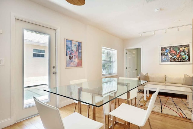 dining space with light wood-style flooring, rail lighting, and baseboards