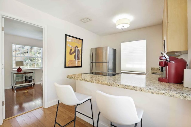 kitchen with baseboards, light stone countertops, light wood-style flooring, a peninsula, and freestanding refrigerator