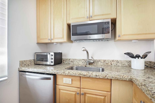 kitchen featuring light stone countertops, a toaster, light brown cabinetry, a sink, and appliances with stainless steel finishes