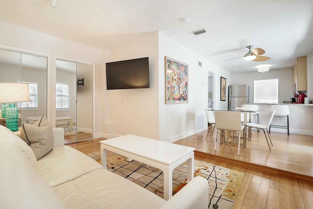 living room featuring light wood finished floors, visible vents, baseboards, and ceiling fan