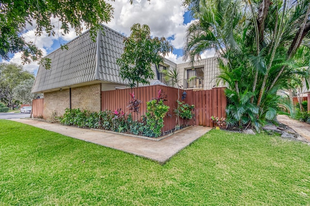 view of property exterior featuring mansard roof, brick siding, fence, a yard, and a tiled roof