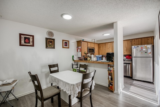 dining space with a textured ceiling, wood finished floors, and baseboards