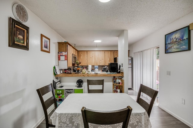 dining room with a textured ceiling, baseboards, and wood finished floors