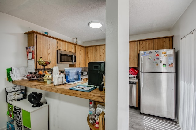 kitchen with light wood finished floors, brown cabinets, stainless steel appliances, a textured ceiling, and light countertops