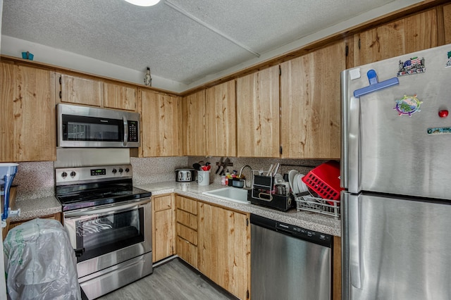 kitchen with a textured ceiling, a sink, light countertops, appliances with stainless steel finishes, and light wood-type flooring