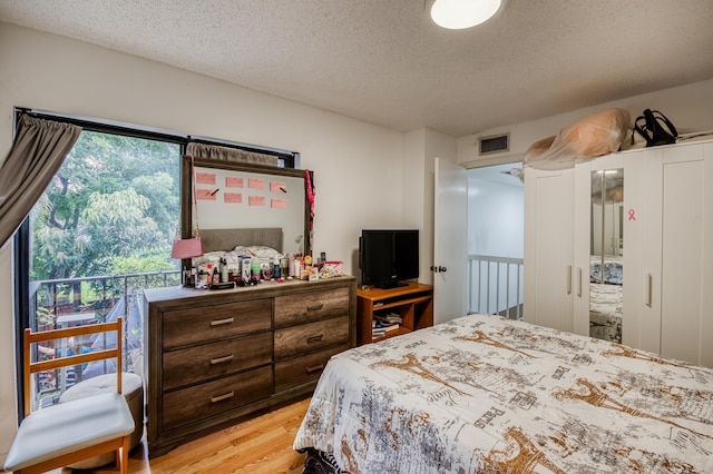 bedroom with light wood finished floors, visible vents, and a textured ceiling