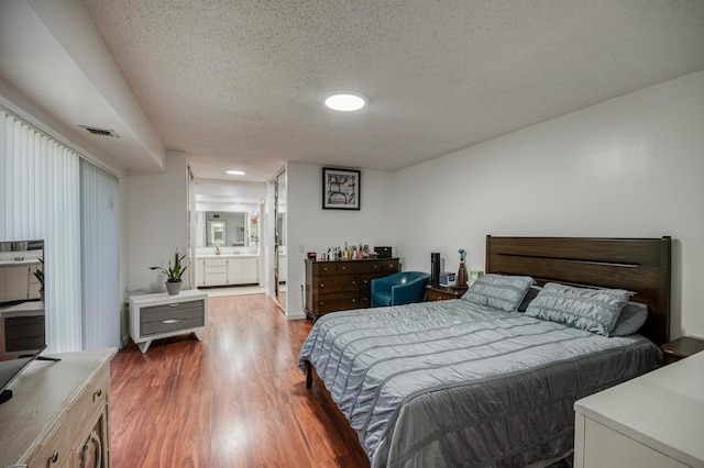 bedroom with visible vents, a textured ceiling, ensuite bath, and wood finished floors