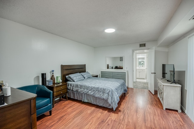 bedroom featuring visible vents, a textured ceiling, baseboards, and wood finished floors