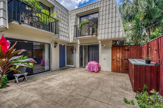 rear view of property featuring a patio, mansard roof, fence, a tiled roof, and stucco siding