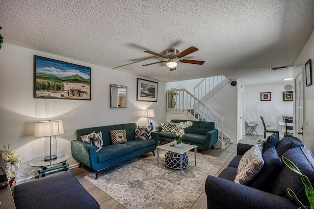 living area with visible vents, ceiling fan, stairway, wood finished floors, and a textured ceiling