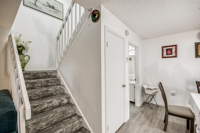 staircase featuring a textured ceiling, baseboards, and wood finished floors