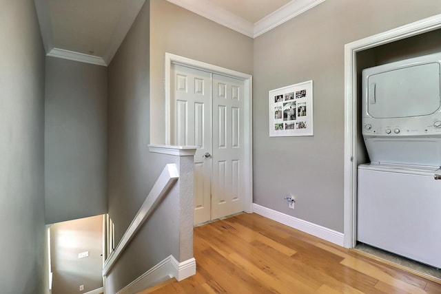 laundry area featuring laundry area, baseboards, stacked washer / drying machine, light wood finished floors, and crown molding