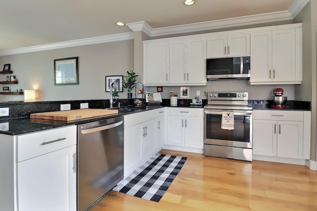 kitchen featuring appliances with stainless steel finishes, ornamental molding, white cabinets, a sink, and a peninsula