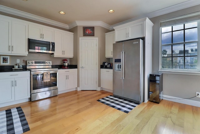 kitchen with light wood-style floors, appliances with stainless steel finishes, white cabinets, and ornamental molding