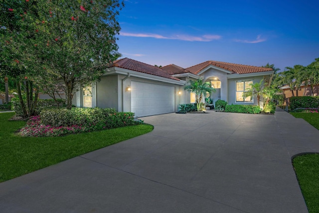 mediterranean / spanish-style house with stucco siding, a lawn, driveway, a tile roof, and an attached garage