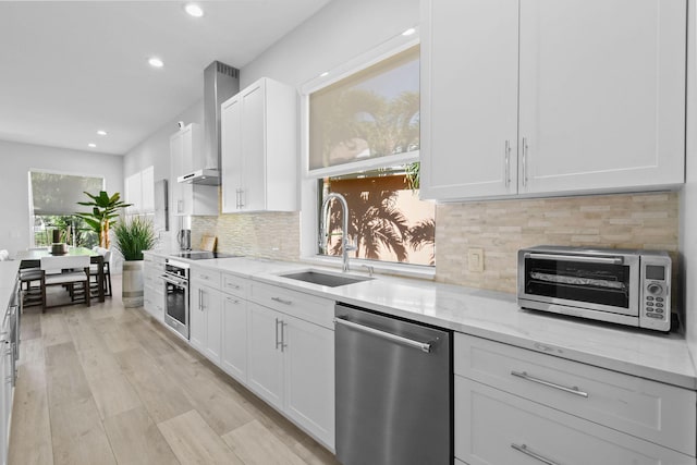 kitchen with light stone countertops, a toaster, appliances with stainless steel finishes, wall chimney exhaust hood, and a sink