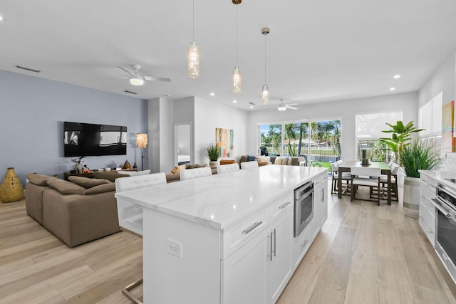 kitchen featuring visible vents, open floor plan, light wood-type flooring, light stone counters, and white cabinetry