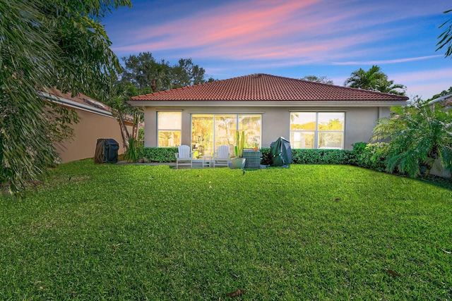 rear view of house featuring a lawn, a tiled roof, and stucco siding