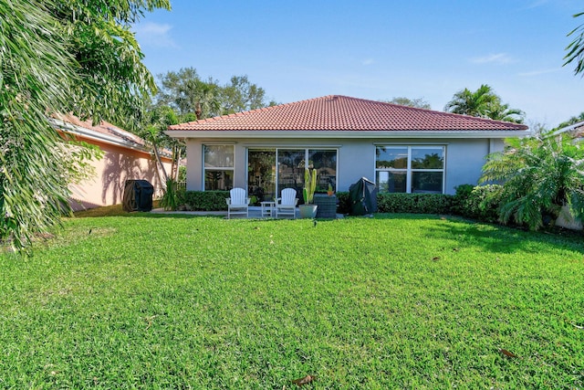 rear view of property featuring a tiled roof, a lawn, and stucco siding