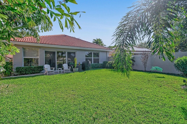 back of property with a yard, fence, a tile roof, and stucco siding