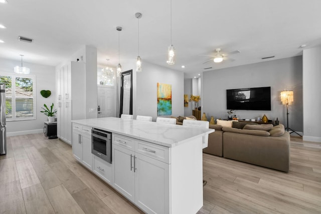 kitchen with light wood-style flooring, a center island, white cabinetry, appliances with stainless steel finishes, and light stone countertops