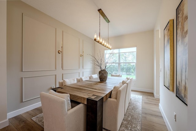 dining room with a chandelier, a decorative wall, baseboards, and light wood-style floors