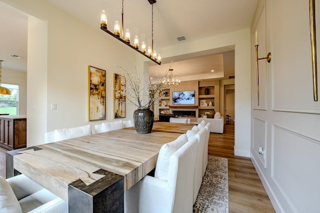 dining area with built in shelves, a fireplace, visible vents, light wood-style flooring, and a chandelier